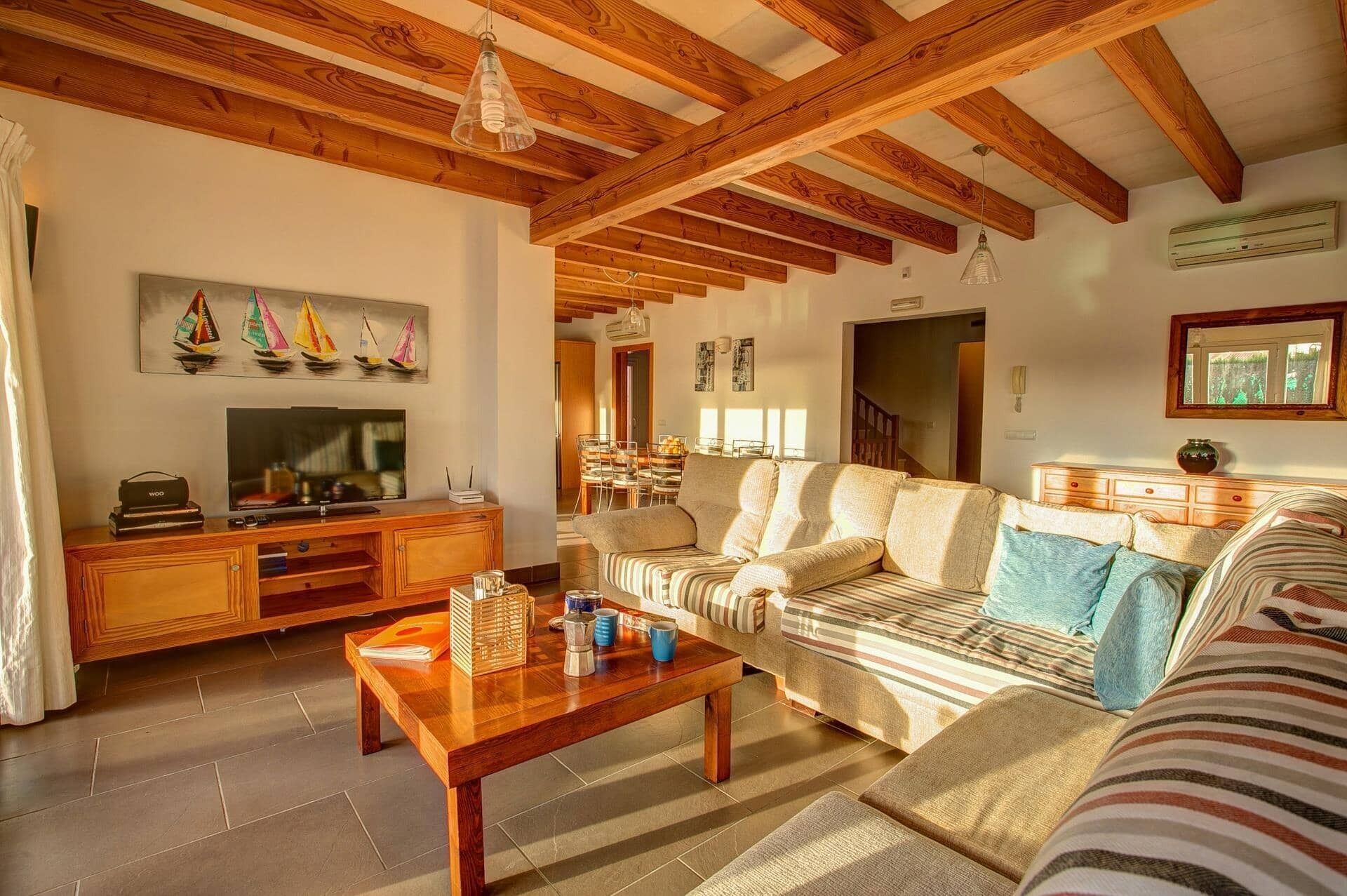 A living room with a wooden ceiling, a sofa, a coffee table, a TV, and a painting of sailboats.