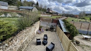 Une terrasse de jardin aménagée avec du mobilier d’extérieur, un mur en pierre et une vue sur un quartier résidentiel.