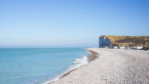 Une plage de galets, avec une falaise et un ciel dégagé.