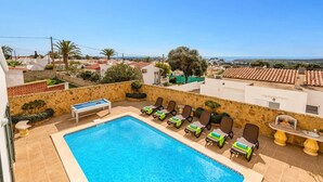 A pool area with lounge chairs and a table, surrounded by stone walls and a view of the sea and buildings. - Villa Sidanya by Villa Plus (Cala en Porter)