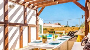 An outdoor dining area with a pool, wooden pergola, and stone wall. - Villa Sidanya by Villa Plus (Cala en Porter)