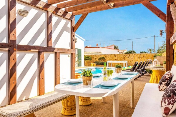 An outdoor dining area with a pool, wooden pergola, and stone wall.