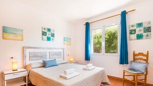 A bedroom with a large bed, two bedside tables, a chair, and a window with curtains. - Villa Sirenita by Villa Plus (Los Delfines)