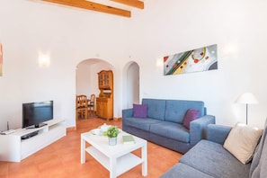 A living room with a TV, sofa, coffee table, and a painting on the wall.