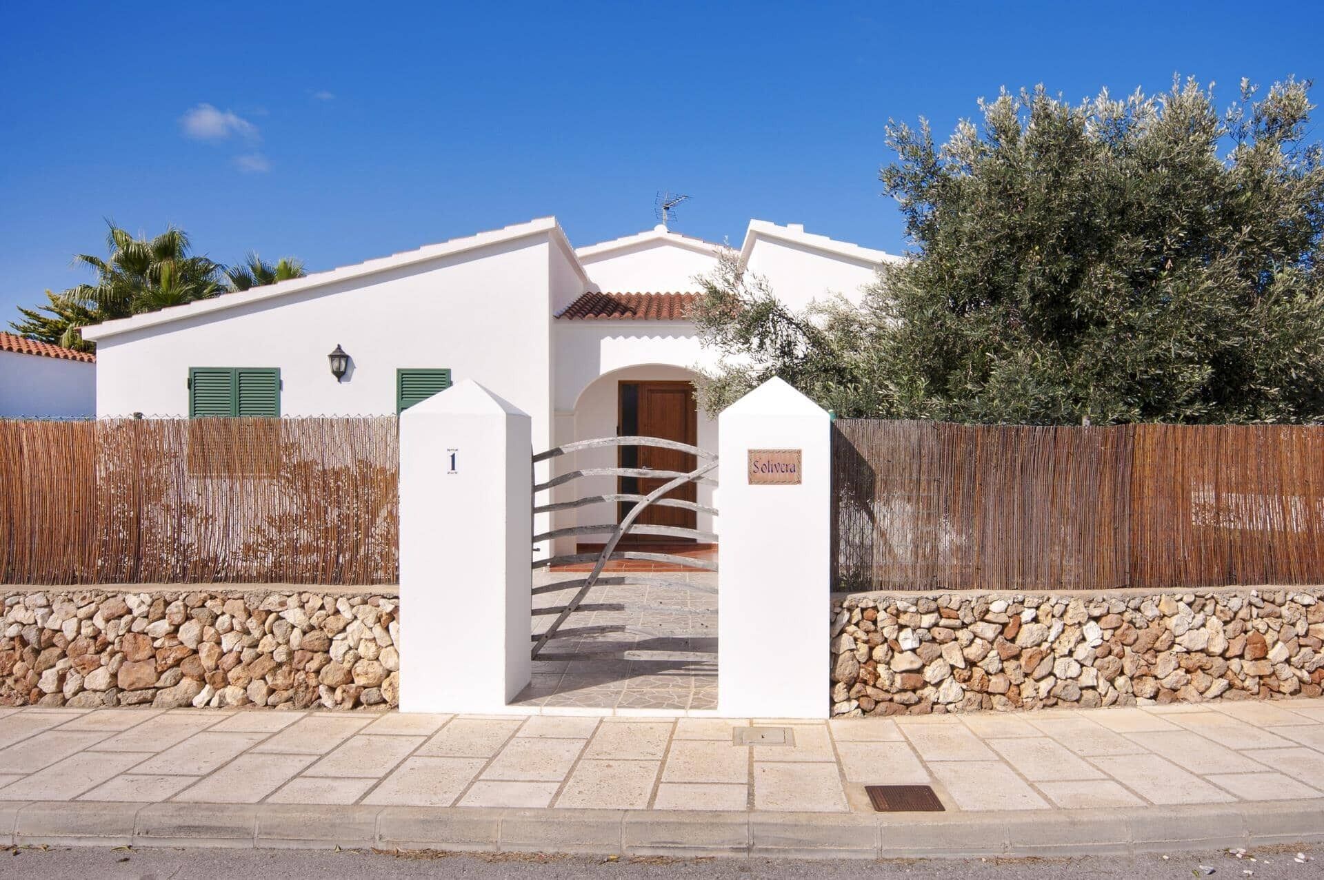 A white building with a stone wall, a wooden gate, and a sign reading 'Solivera.'