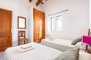 Een slaapkamer met twee bedden, een houten garderobe, een stoel en een raam met gordijnen.