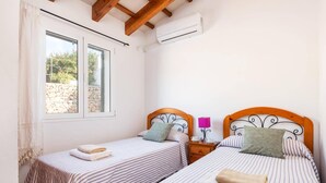 Une chambre avec deux lits simples, une fenêtre, un appareil de climatisation et une table de chevet avec une lampe.