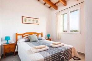 Un letto rifatto con una coperta a motivi, due abat-jour, un quadro incorniciato al muro e una finestra con tende.