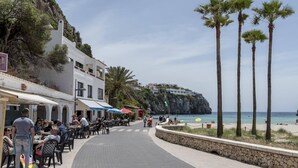 Eine Küstenstraße mit Außenbestuhlung, Palmen und Blick auf den Strand.