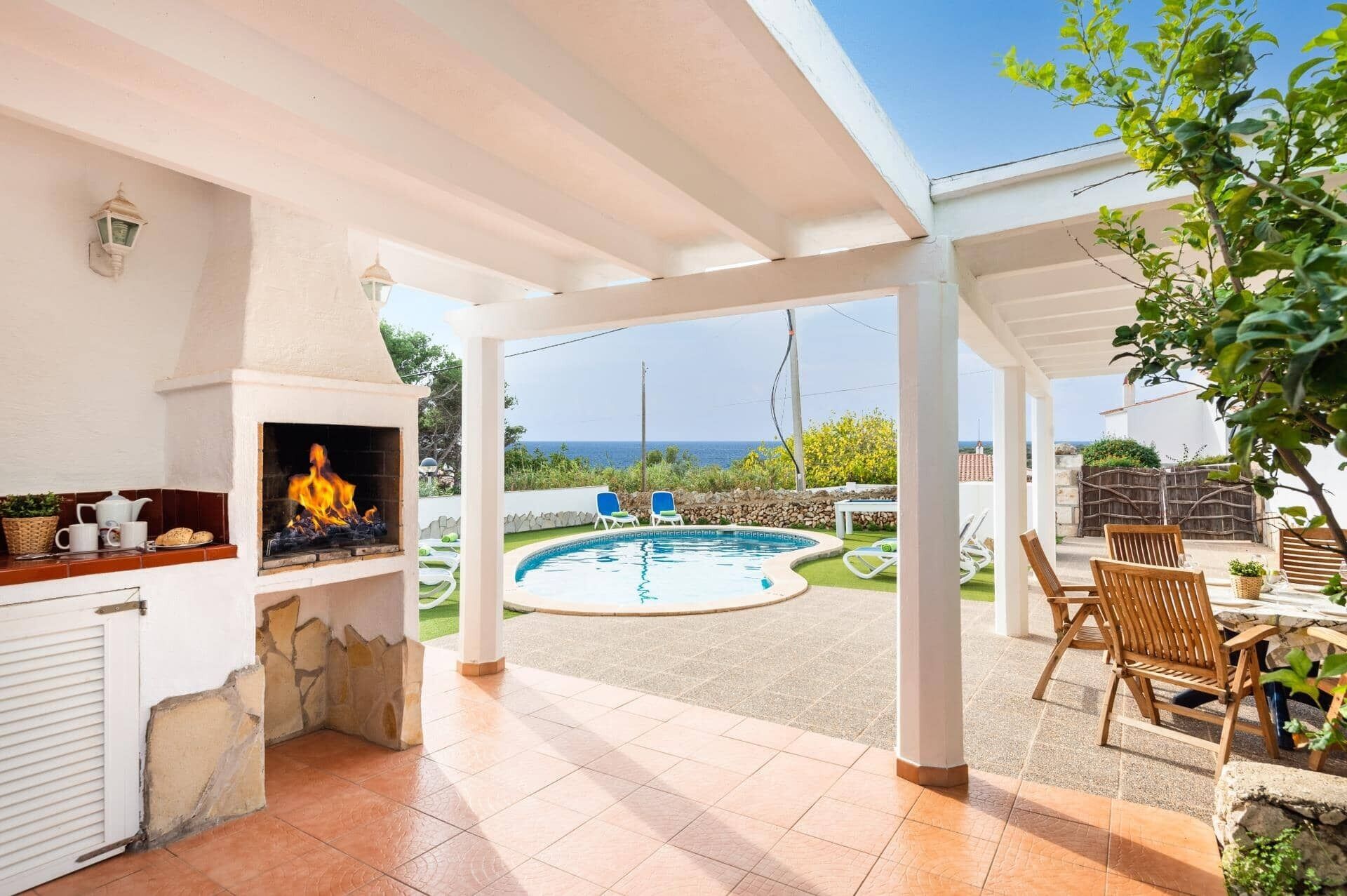 A covered outdoor area with a pool, lounge chairs, and a fireplace.