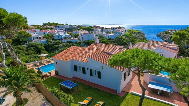 Eine Küstenvilla mit Pool, umgeben von üppiger Vegetation und freiem Blick aufs Meer.