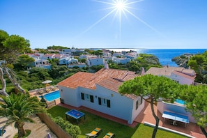 Rannalla sijaitseva huvila, jossa on uima-allas, ja sen ympärillä on vehreää kasvillisuutta sekä avoin näkymä merelle.