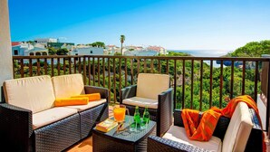 Ein Balkon mit Korbmöbeln, einem Tisch mit Getränken und Blick auf das Meer und die Gebäude.