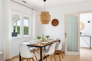 A dining area with a table set for four, white chairs, a wooden table, and a hanging woven light fixture.
