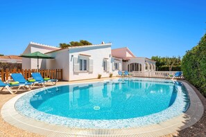 A poolside area with a clear blue pool, lounge chairs, and a white building with a tiled roof. - Villa Mar Clara by Villa Plus (Ciutadella de Menorca)