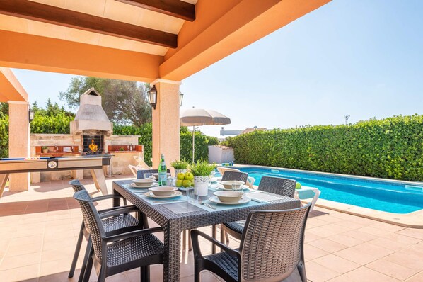 Un espace extérieur aménagé pour les repas, avec une piscine, un barbecue et une haie bien entretenue.