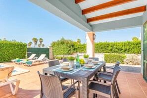 An outdoor patio with a dining table set for four, surrounded by wicker chairs, a pool, and lounge chairs.