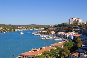A coastal town with a marina, buildings with red-tiled roofs, and a prominent white building on a hill.