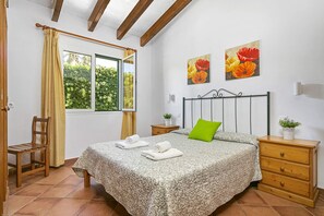 Une chambre à coucher comprenant un lit, une chaise, une table de chevet, une commode et deux fenêtres.