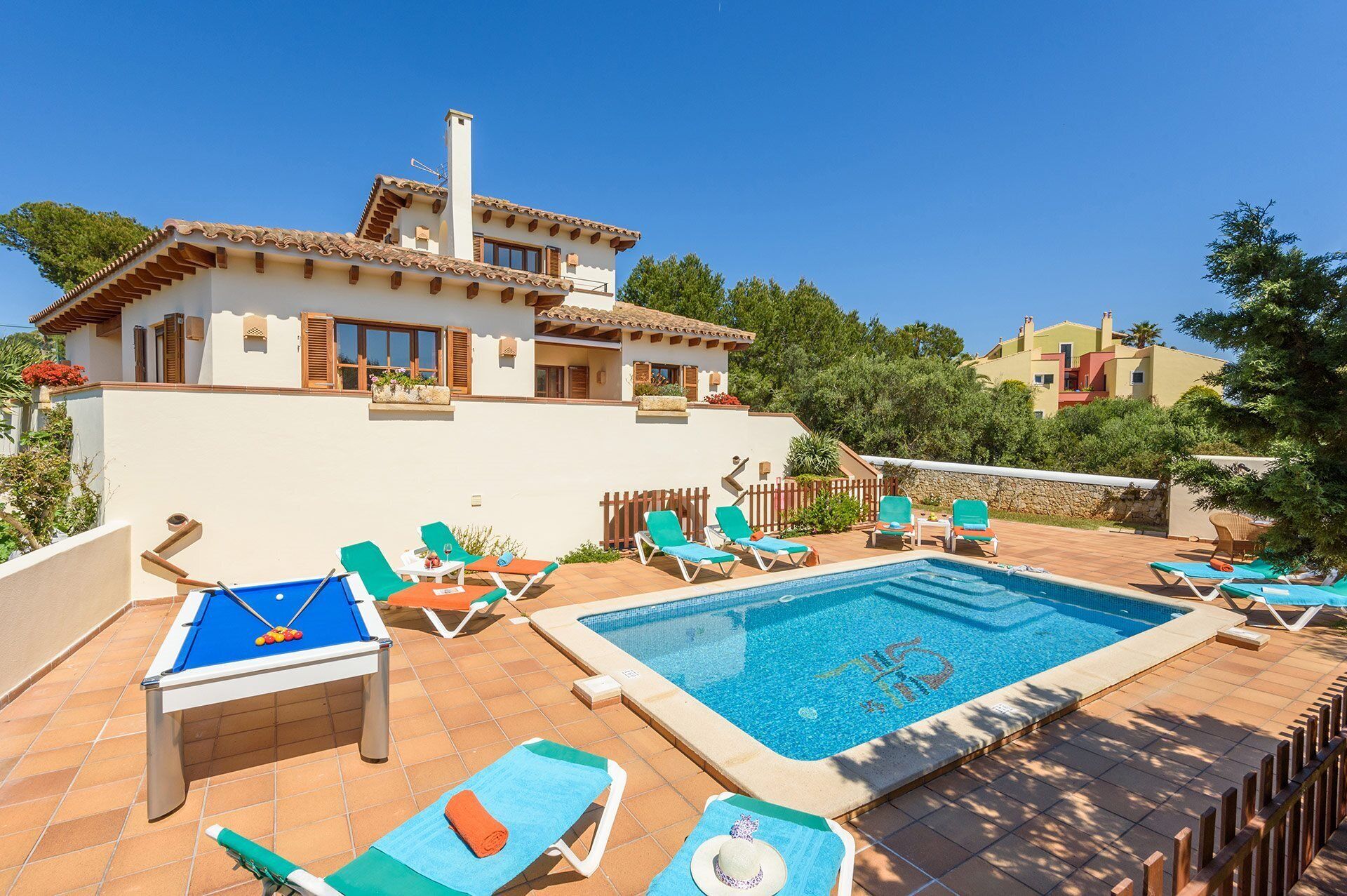 A pool area with lounge chairs, a pool table, and a clear blue sky.