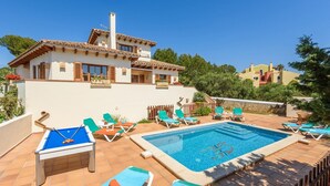 Un área de piscina con sillones reclinables, mesa de billar y cielo azul despejado.