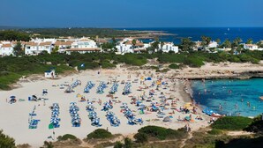 Una playa con numerosos sombrillas y gente, rodeada de edificios y un mar azul cristalino.