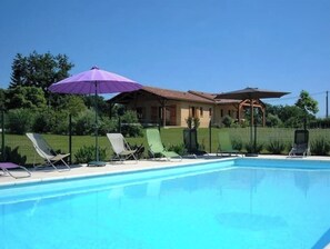Une piscine entourée d’une clôture et de verdure, avec des chaises longues et des parasols.