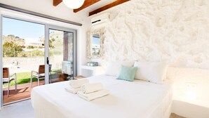 Un dormitorio con una cama grande, una pared de piedra y vistas a un jardín por una puerta corredera.