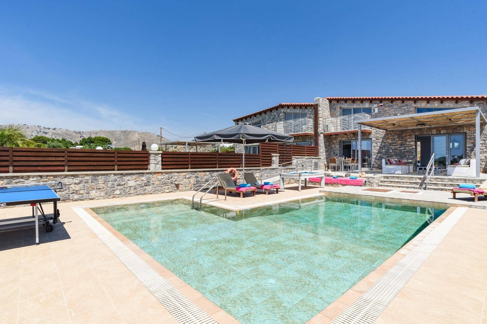 Ein Poolbereich mit Liegestühlen, einem Tisch und einem Steinhaus mit Balkon.