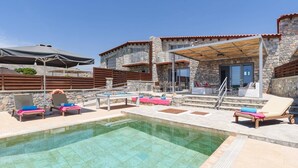 Un área de piscina con sillones de descanso, una mesa y una zona de estar techada.
