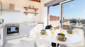 Una cocina moderna con horno empotrado, un lavaplatos y una zona de comedor con una mesa dispuesta para dos.