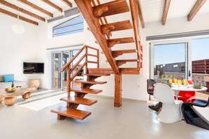 A modern interior with a wooden spiral staircase, a dining area with a table and chairs, and a TV mounted on the wall.