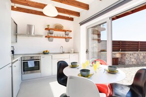 A modern kitchen with a built-in oven, a dining area with a round table and chairs, and a large sliding glass door leading to an outdoor patio. - Villa Alcyone Seastone by Villa Plus (Rhodes)