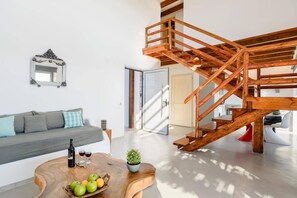 A modern living room with a wooden staircase, a sofa, a coffee table with fruits and wine, and a mirror on the wall.