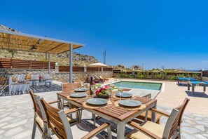 A poolside dining area with a table set for four, surrounded by stone walls and a view of the sea. - Villa Dione Seastone by Villa Plus (Rhodes)
