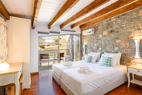 A bedroom with two beds, a stone wall, and a view of the outdoors.