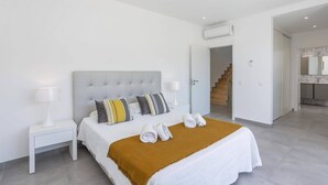 Un dormitori modern amb un reposacapses amb textura, roba de llit blanca i una manta marró.