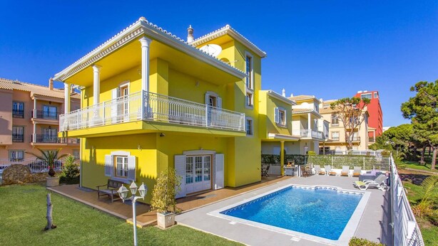 Un bâtiment jaune à deux étages, doté d’une piscine, d’un espace extérieur aménagé et d’un jardin.