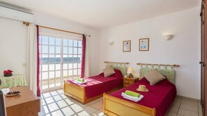 A room with two beds, a desk, a window with curtains, and a view of the sea. - Villa Colina do Sol by Villa Plus (Paderne)