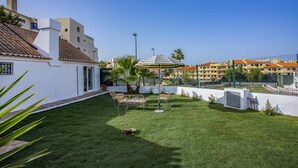 A well-maintained garden with a lawn, a striped umbrella, and a white building with shutters. - Villa Casa Calma by Villa Plus (Albufeira)