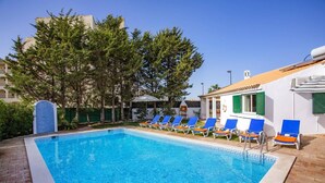 A swimming pool with blue water, surrounded by lounge chairs and a building with a tiled roof. - Villa Casa Calma by Villa Plus (Albufeira)