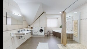 Een moderne badkamer met een ingebouwde wasmachine, een grote spiegel, een bad en een douchegordijn.