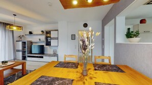 Een moderne woonkamer met een houten eettafel, twee stoelen, een televisie en een decoratieve vaas met gedroogde bloemen.