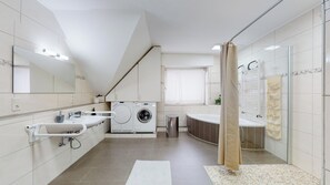 Ein modernes Badezimmer mit integrierter Waschmaschine, einem großen Spiegel, einer Badewanne und einer Duschvorhang.