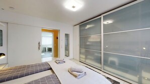 Een moderne slaapkamer met een grote schuifpui, een bed met een grijs-wit beddegoed en een klein nachtkastje.