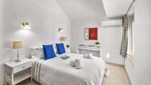 Ein Schlafzimmer mit einem Bett, Nachttischen, einem Schreibtisch, einem Spiegel und einer Klimaanlage.