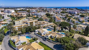 Eine Vogelperspektive auf Villa Pinheiro Oura, die einen Wohnbereich mit mehreren Gebäuden, einem markanten Pool und freiem Blick aufs Meer zeigt.