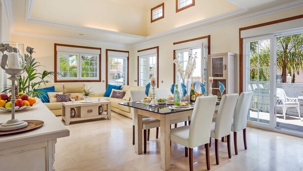 A spacious living area with a dining table, comfortable seating, and large windows offering a view of the outdoors.