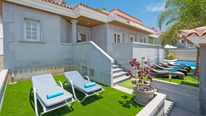A poolside area with lounge chairs, a small pool, and a staircase leading to a building with a tiled roof.