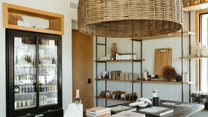 Un interior moderno con una mesa negra en el centro, una lámpara colgante de mimbre y estantes con diversos objetos.